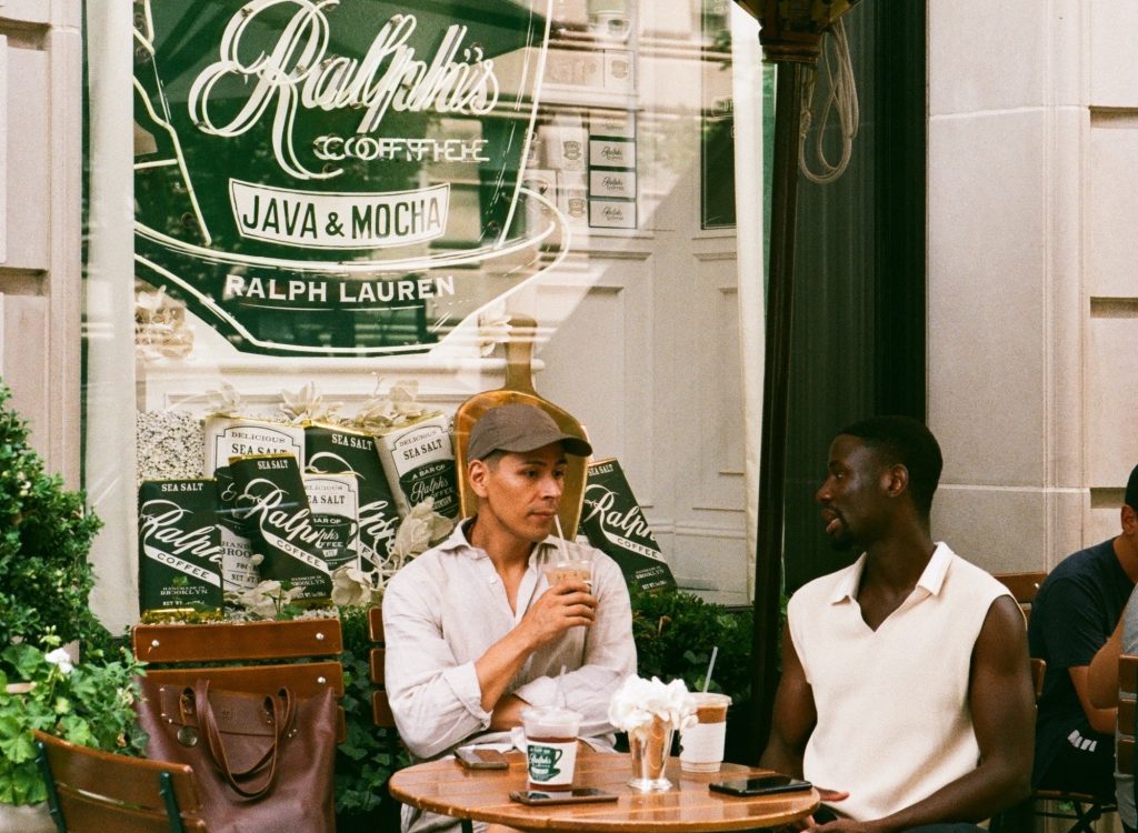 two men drinking coffee in front of a cafe