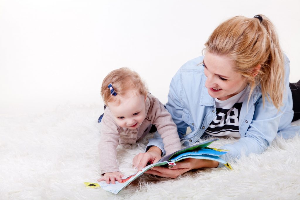幼兒發展，俯臥在地，開心地看著書本，母親在一旁陪伴