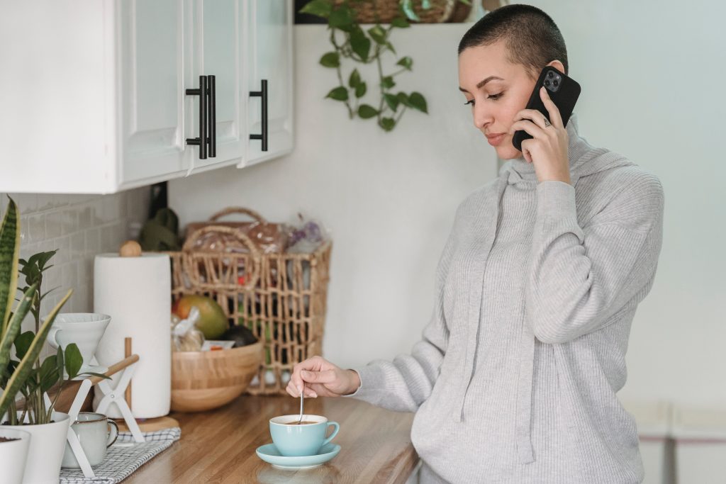 Short haired woman talking on the phone while preparing her coffee