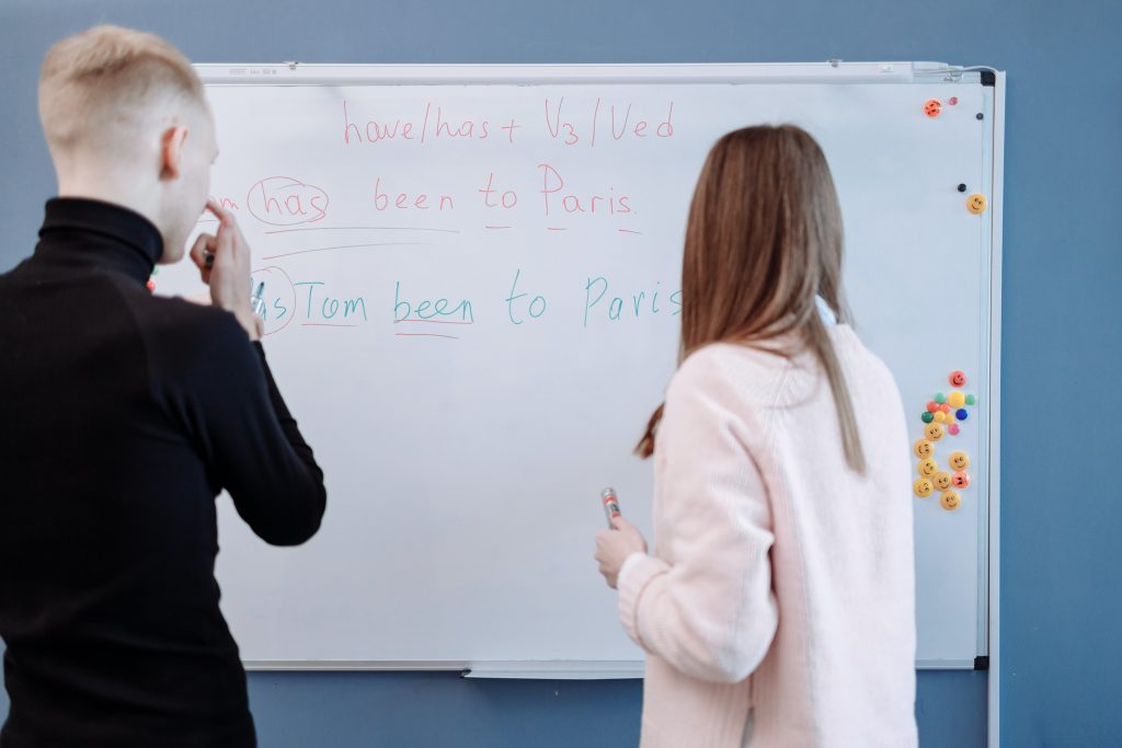 A student and a teacher standing in front of a white board discussing to be verbs
